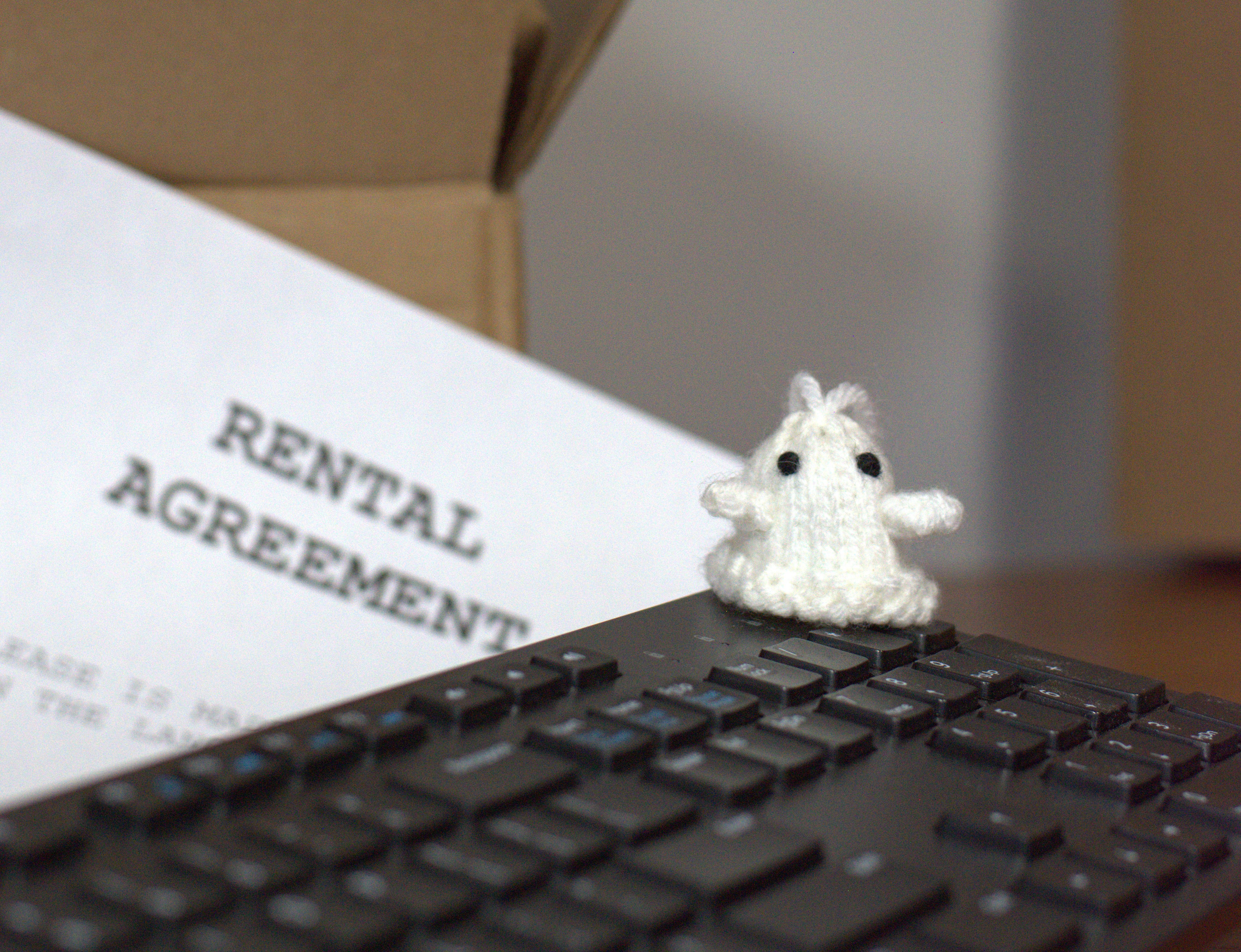 An adorable ghost doll is placed on a  keyboard. A rental agreement is placed strategically in the background